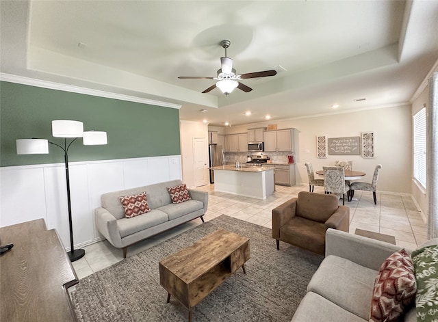 living room featuring ceiling fan, light tile patterned flooring, ornamental molding, and a tray ceiling