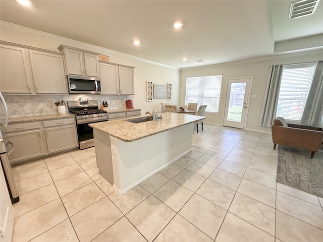 kitchen featuring decorative backsplash, appliances with stainless steel finishes, light stone counters, a kitchen island with sink, and sink