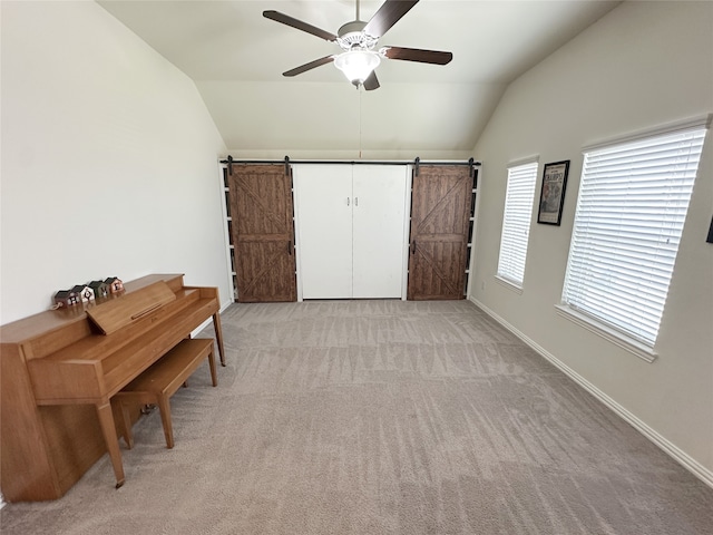 interior space featuring a barn door, light carpet, ceiling fan, and vaulted ceiling