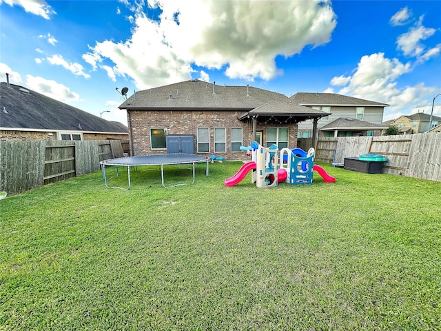 back of property featuring a playground, a yard, and a trampoline