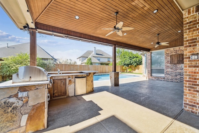 view of patio / terrace with a bar, a fenced in pool, ceiling fan, and exterior kitchen