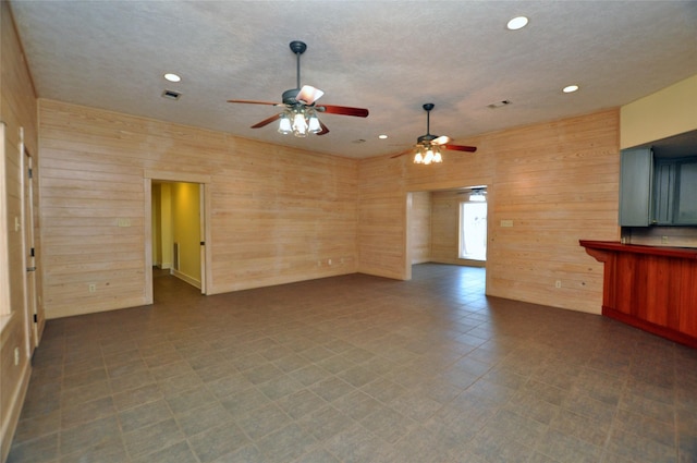 unfurnished living room with visible vents, wooden walls, and a textured ceiling