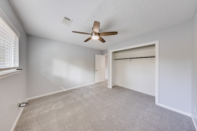 unfurnished bedroom featuring ceiling fan, a closet, light carpet, and a textured ceiling