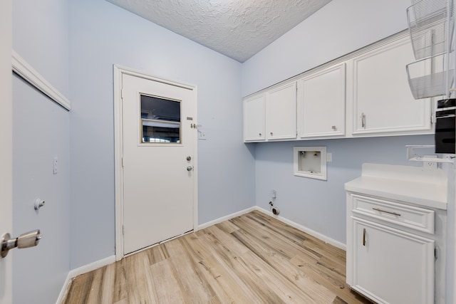 clothes washing area with gas dryer hookup, cabinets, light hardwood / wood-style flooring, washer hookup, and a textured ceiling