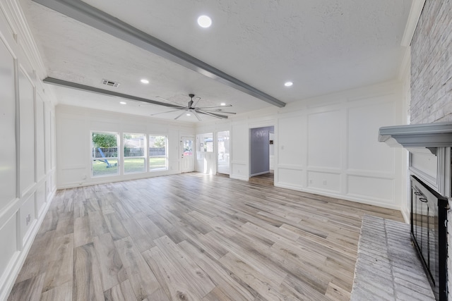 unfurnished living room featuring ceiling fan, light hardwood / wood-style flooring, beamed ceiling, a textured ceiling, and a fireplace