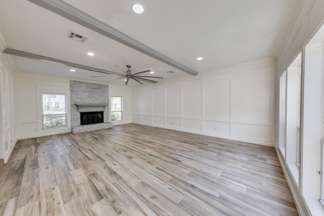 unfurnished living room featuring beam ceiling, ceiling fan, a large fireplace, crown molding, and light wood-type flooring