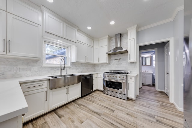 kitchen with sink, stainless steel appliances, wall chimney range hood, crown molding, and white cabinets