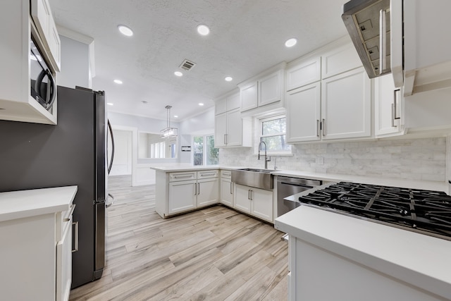 kitchen with kitchen peninsula, stainless steel appliances, sink, white cabinetry, and hanging light fixtures