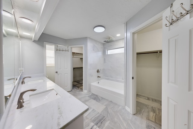 bathroom with a textured ceiling, vanity, and tiled shower / bath