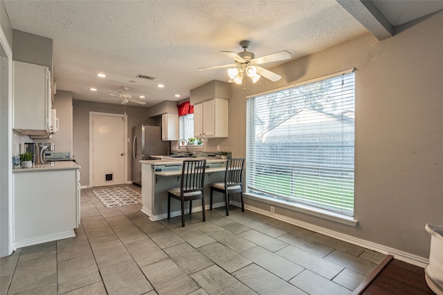 kitchen with ceiling fan, stainless steel fridge, white cabinetry, and a textured ceiling