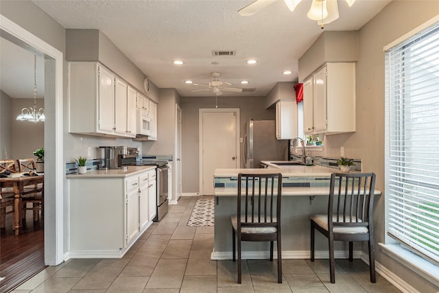 kitchen with kitchen peninsula, appliances with stainless steel finishes, ceiling fan with notable chandelier, sink, and white cabinetry