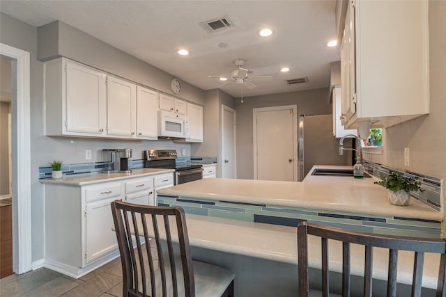 kitchen featuring white cabinets, tile patterned floors, ceiling fan, kitchen peninsula, and stainless steel appliances