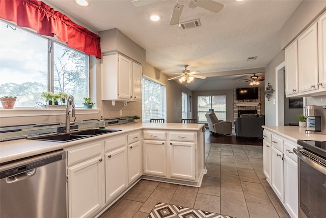 kitchen featuring sink, a brick fireplace, white cabinetry, kitchen peninsula, and stainless steel appliances