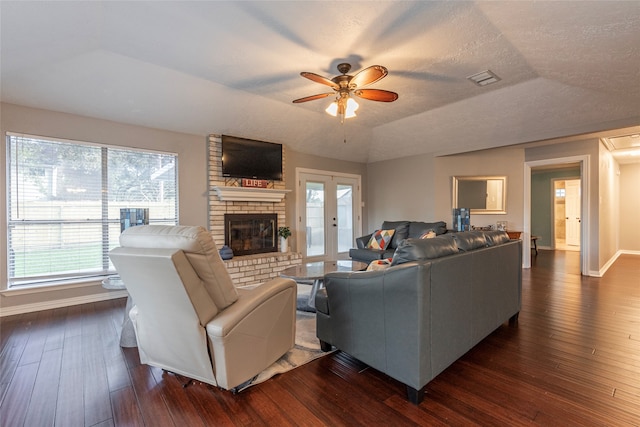 living room featuring ceiling fan, french doors, dark wood-type flooring, a brick fireplace, and a textured ceiling