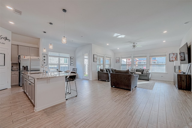 kitchen with light wood-type flooring, gray cabinetry, ceiling fan, a breakfast bar area, and an island with sink