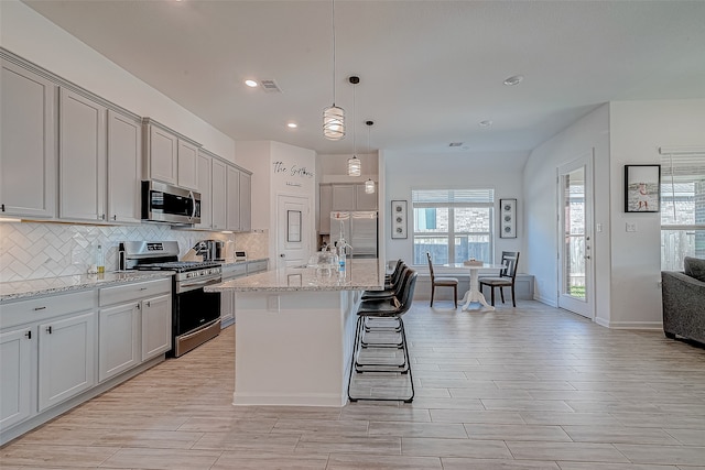 kitchen featuring pendant lighting, a center island with sink, a kitchen breakfast bar, light stone countertops, and stainless steel appliances