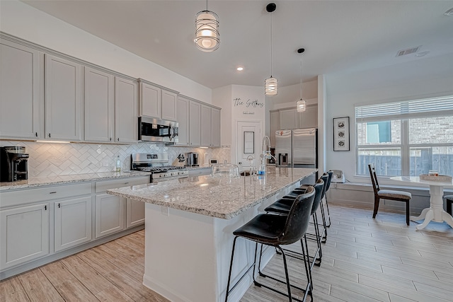 kitchen with a center island with sink, light hardwood / wood-style floors, stainless steel appliances, and hanging light fixtures