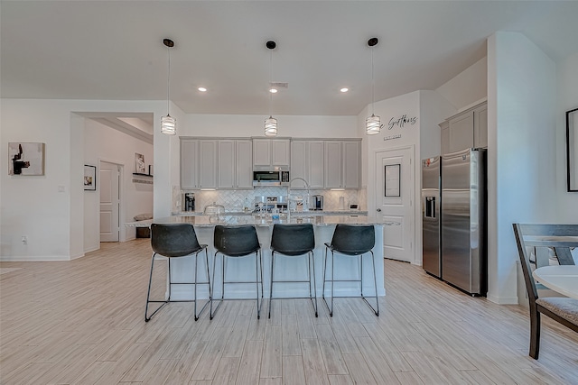 kitchen with gray cabinets, an island with sink, hanging light fixtures, and appliances with stainless steel finishes