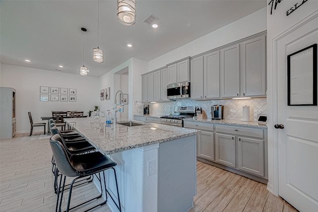 kitchen featuring sink, hanging light fixtures, gray cabinets, a kitchen island with sink, and appliances with stainless steel finishes