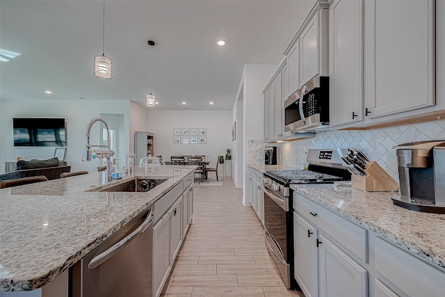 kitchen with white cabinetry, light stone counters, pendant lighting, a kitchen island with sink, and appliances with stainless steel finishes