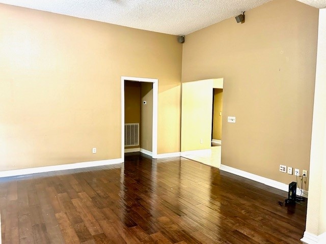 empty room with a towering ceiling, dark hardwood / wood-style floors, and a textured ceiling