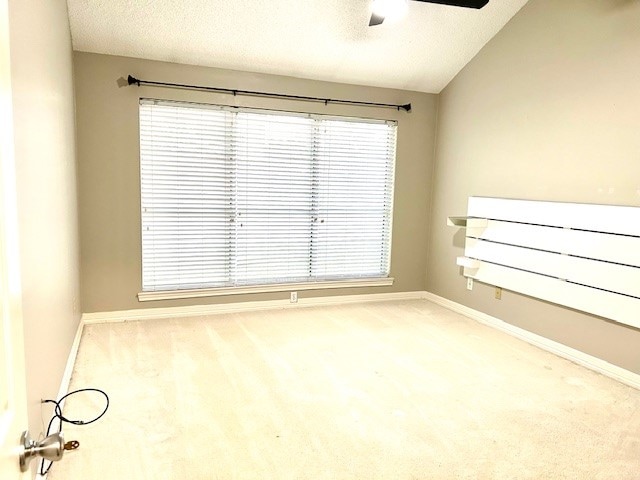 carpeted empty room featuring a wealth of natural light, a textured ceiling, ceiling fan, and lofted ceiling