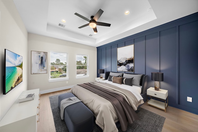 bedroom featuring ceiling fan, light wood-type flooring, and a tray ceiling