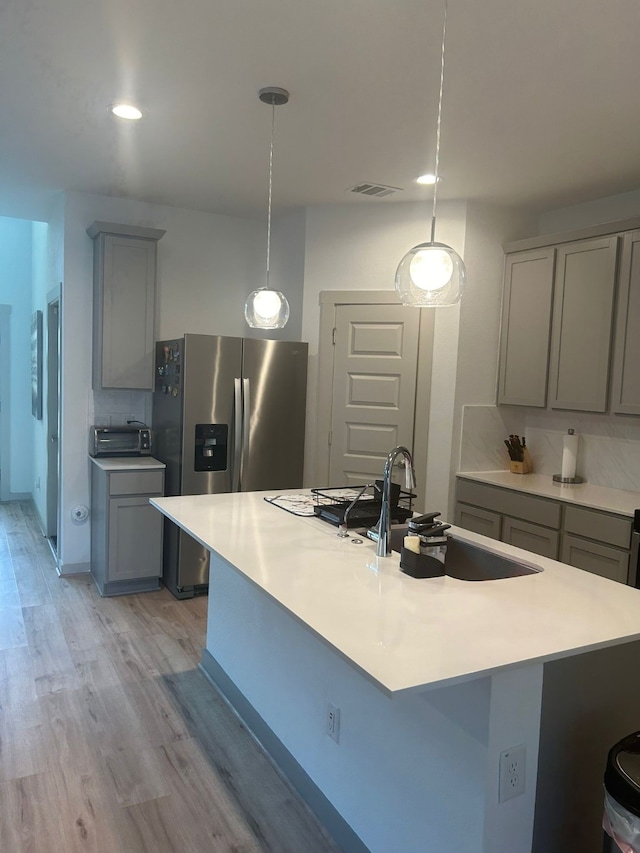 kitchen with stainless steel refrigerator with ice dispenser, tasteful backsplash, sink, pendant lighting, and light hardwood / wood-style floors