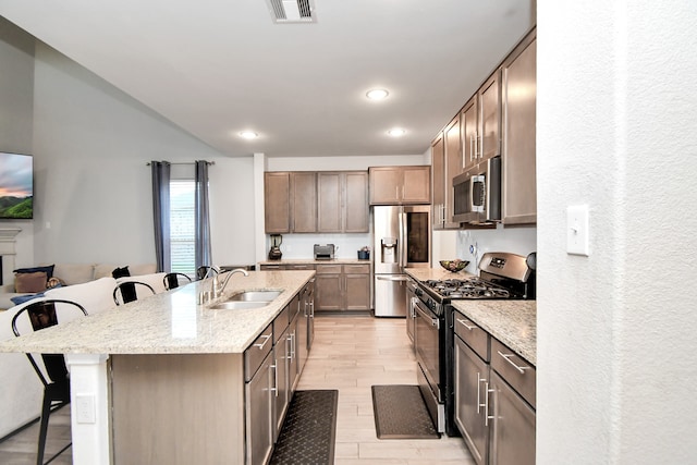 kitchen with sink, stainless steel appliances, a breakfast bar area, a kitchen island with sink, and light wood-type flooring