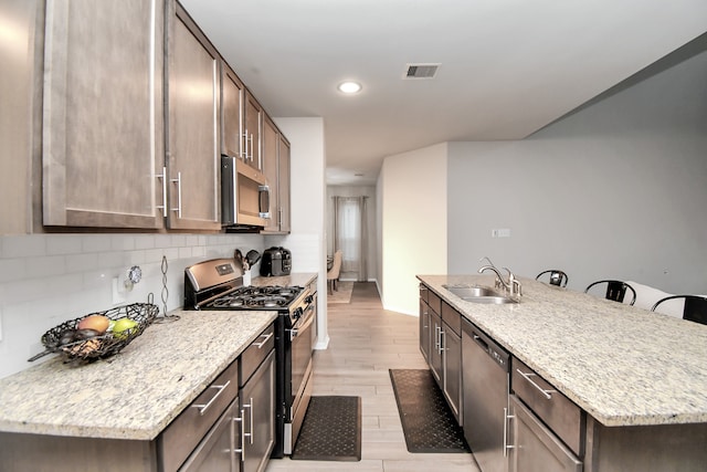 kitchen with light stone countertops, stainless steel appliances, a kitchen island with sink, sink, and light hardwood / wood-style flooring