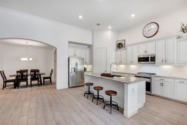 kitchen with white cabinetry, sink, stainless steel appliances, light hardwood / wood-style flooring, and an island with sink