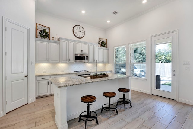 kitchen featuring a center island with sink, white cabinetry, ornamental molding, and light stone counters