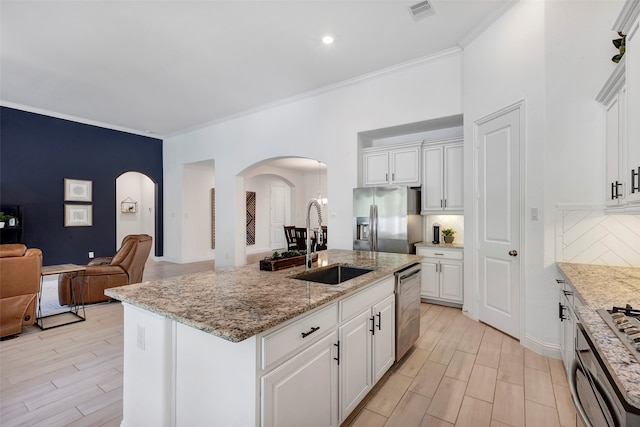 kitchen featuring appliances with stainless steel finishes, backsplash, sink, a center island with sink, and white cabinetry