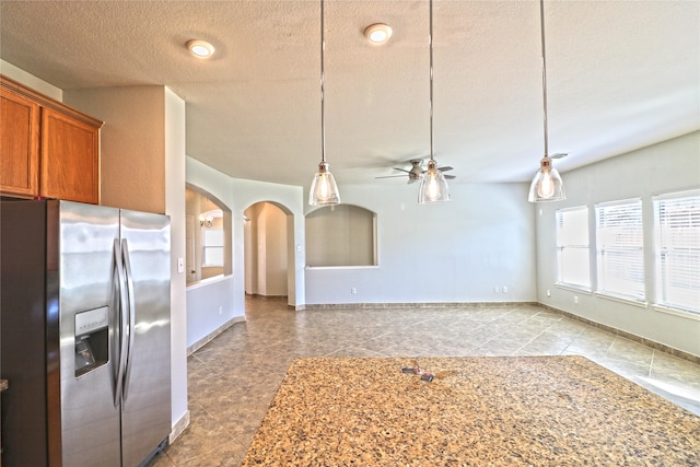 kitchen with stainless steel refrigerator with ice dispenser, a textured ceiling, ceiling fan, and pendant lighting