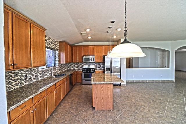 kitchen featuring stainless steel appliances, vaulted ceiling, pendant lighting, dark stone countertops, and a center island