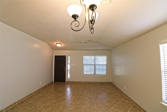 unfurnished room featuring dark tile patterned flooring, a healthy amount of sunlight, lofted ceiling, and a notable chandelier