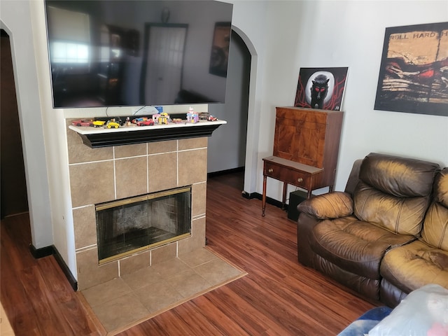 living room with a tile fireplace and dark wood-type flooring