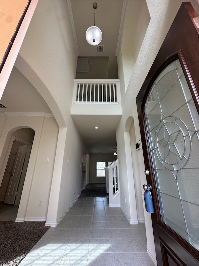 entryway featuring a high ceiling, light tile patterned floors, and ornamental molding