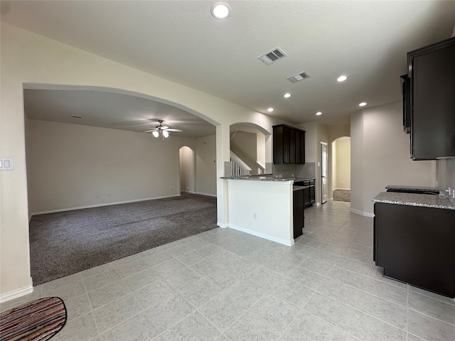 kitchen with ceiling fan, light colored carpet, and light stone counters