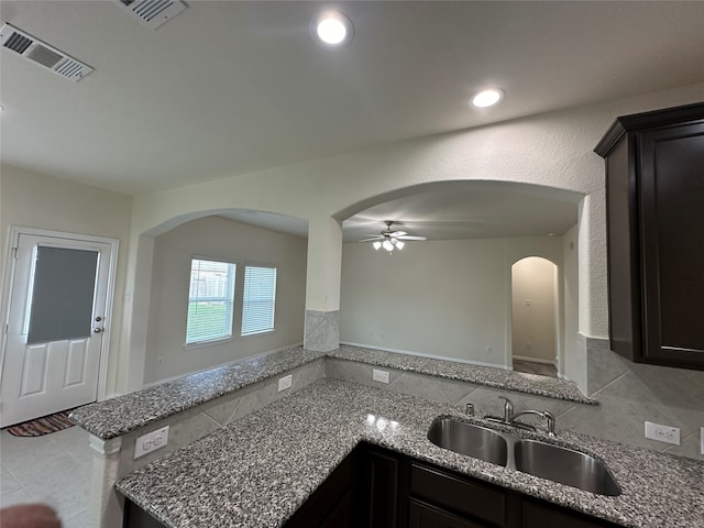 kitchen with ceiling fan, dark brown cabinetry, light stone countertops, and sink