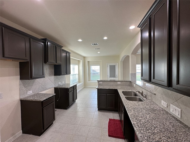 kitchen with sink, tasteful backsplash, kitchen peninsula, dark stone counters, and light tile patterned floors