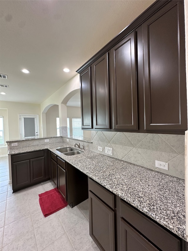 kitchen featuring tasteful backsplash, light stone counters, dark brown cabinetry, sink, and light tile patterned flooring