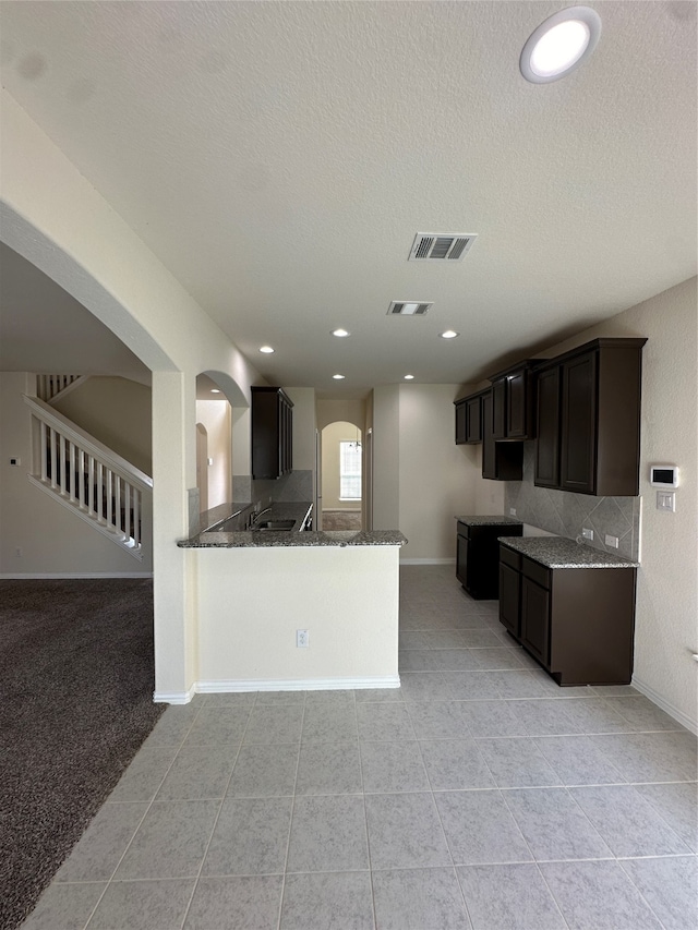 kitchen with kitchen peninsula, dark stone countertops, a textured ceiling, dark brown cabinets, and light tile patterned floors