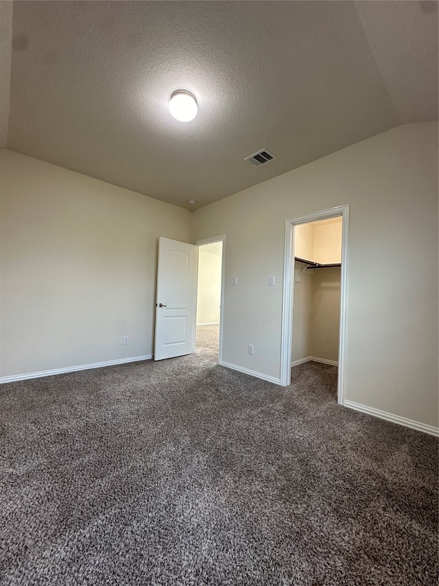 unfurnished bedroom with dark colored carpet, lofted ceiling, a textured ceiling, a walk in closet, and a closet