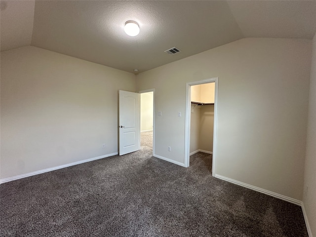 unfurnished bedroom with a walk in closet, a closet, lofted ceiling, and dark colored carpet