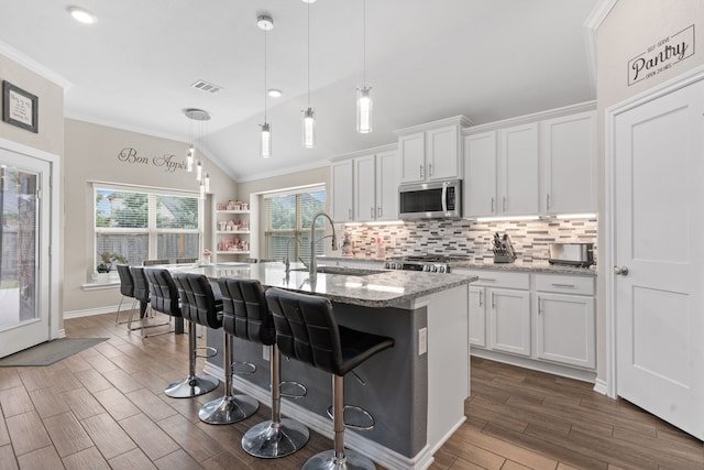 kitchen with decorative light fixtures, vaulted ceiling, a center island with sink, and white cabinetry