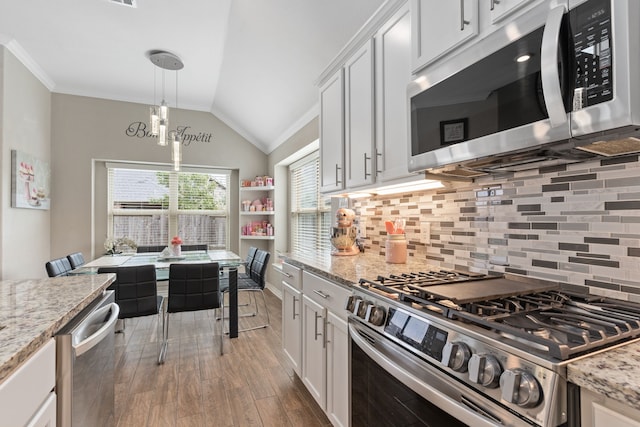 kitchen featuring pendant lighting, lofted ceiling, white cabinets, light stone counters, and stainless steel appliances