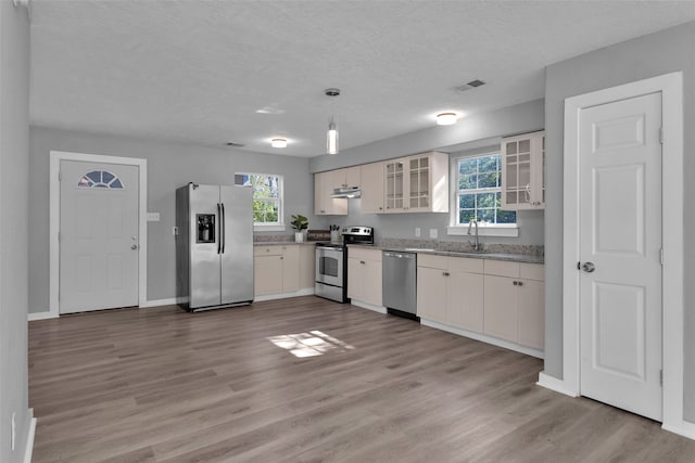 kitchen with sink, light wood-type flooring, decorative light fixtures, and appliances with stainless steel finishes