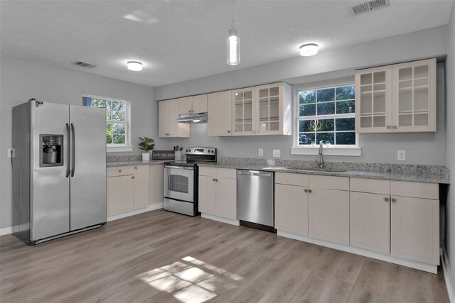 kitchen featuring sink, hanging light fixtures, light stone counters, light hardwood / wood-style flooring, and appliances with stainless steel finishes