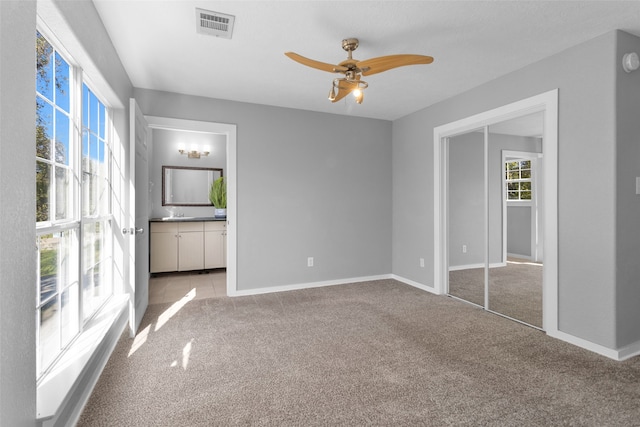 unfurnished bedroom with light carpet, connected bathroom, a closet, and ceiling fan